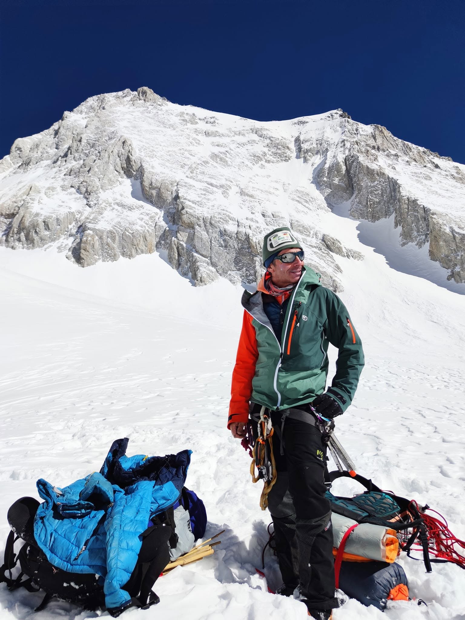 Alpinista in tenuta da alta quota davanti a una parete innevata