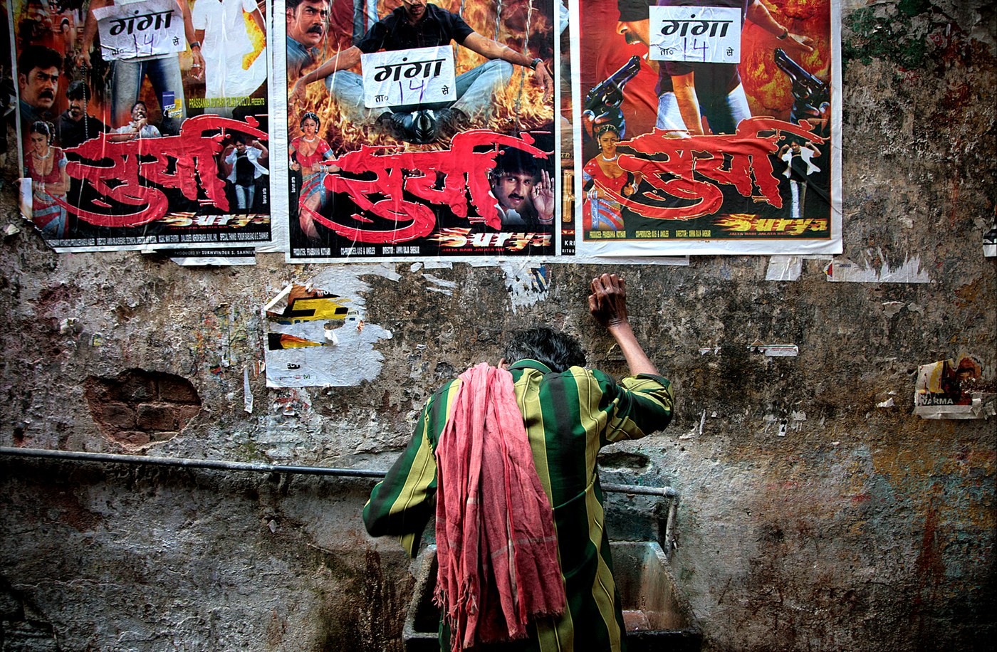 Fotografia di Gino Lazzarin scattata in India: un uomo di spalle affissa manifesti di film su un muro dipinto